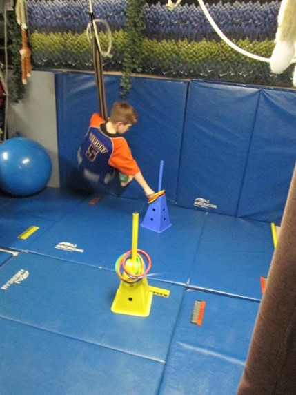 This boy is using a moon swing to pick up a ring from  one stanchion and to place it on another stanchion that is placed further away