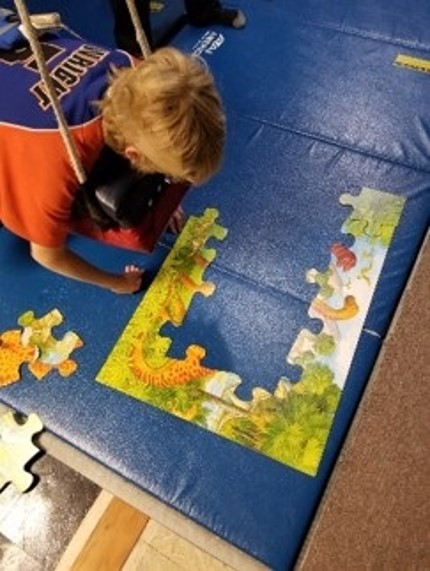 This photo shows a youngster lying on a swing while assembling a puzzle. 