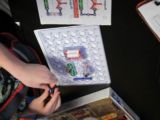 A boy is building an circuit with snaps a  battery and  other parts that snap together