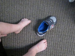 This image shows a boy looking at his feet and a sneaker to see which foot will fit into the sneaker