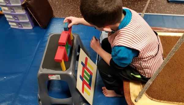 This image shows a boy sitting on a flat swing as he builds a tower of blocks