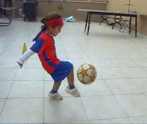 This is an  image of a youngster kicking a soccer ball.  The youngsters’ head is  held in a vertical alignment while the arms and legs engage the soccer ball. 