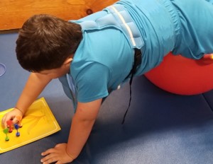 This image of a boy who is prone lying over a physioball is strengthening his back while using sticky darts to form a flower 