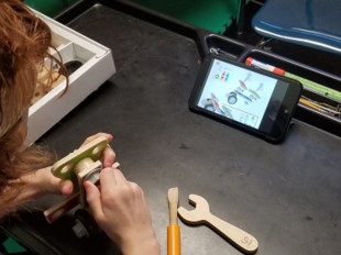 This is a photo of a boy who is using tools to build an airplane from a construction toy as shown on the tablet