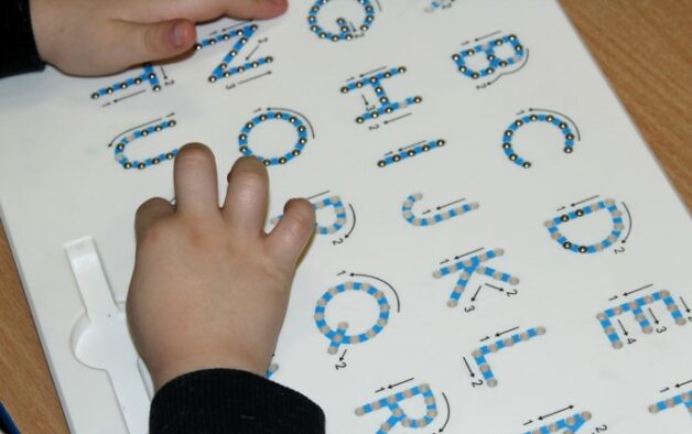 This photo shows a child tracing raised letters of the alphabet