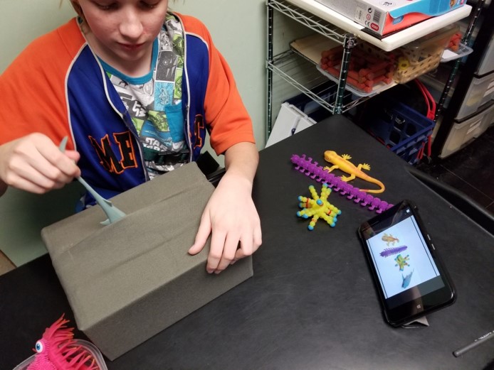 This is an image of a child looking at a screen of rubber animals on a tablet while pulling the tail of one of the animals out of the box