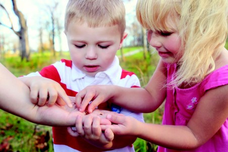 This photo shows two children looking and touching a centipede that is being held in the hand of an adult