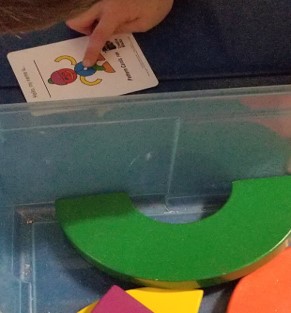 This photo shows a child pointing to the picture of a project to  be assembled with diverse wooden pieces