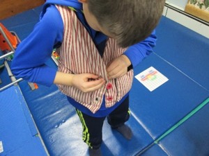 The photo shows a child holds a button hole on one side of a vest with one hand while using the other hand to push a button through the hole