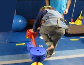 The photo shows a child lifting one leg up to step over an obstacle while standing still and balancing on the other leg