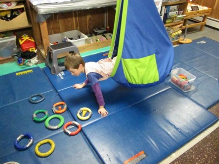 This picture shows a boy who is leaning out of a Fun Zone swing to place a block into rings of matching colors.