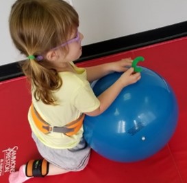 this is a photo of a child kneeling behind an exercise ball while turning a letter “C” into the upright position