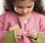 this photo shows a girl who is looking at a button on her sweater.  She is trying to push the button through the hole while using both hands