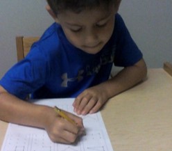 this is a photo of a boy who has positioned himself for handwriting by rotating his right shoulder forward and tilting his head