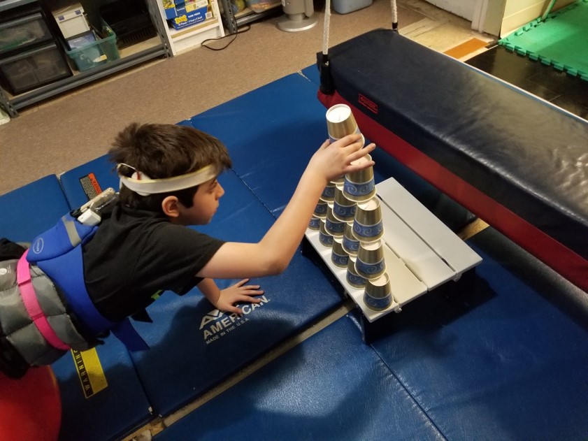 This photo shows a boy performing ball walkouts while stacking a tower of paper cups.  He is using his eyes to carefully guide his hands in placement of each cup