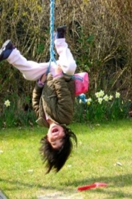 This photo shows a boy hanging upside down and yelling while swinging.
