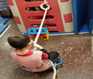 This youngster is sitting on a scooter and pulling on a rope to bring letters to the alphabet house.