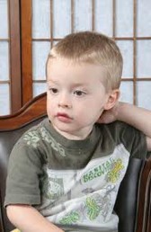 This photo shows a youngster who is passively sitting in a chair with his body draped against it. While he leans against the back of the chair, he is staring vacantly forward and seemingly looking at nothing in particular.