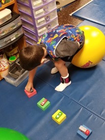 This youngster is using the hop ball to ferry one toy car at a time to position the cars as shown on a task card.