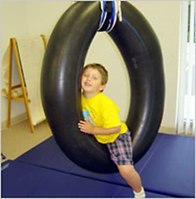 The photo shows a boy who is sitting astride a tire swing. He is using the side of the swing to prop his head and upper body. His body posture lacks signs of initiative to engage an activity.