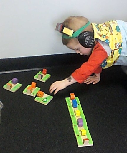 This photo shows a child setting up a row of car/truck dominoes while performing Physioball walk outs.