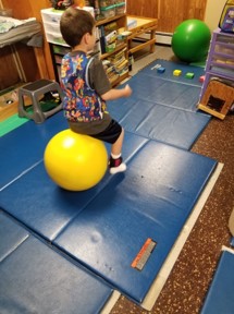 This youngster is using the hop ball to ferry one toy car at a time to position the cars as shown on a task card.