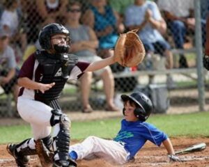 The photo shows two boys playing baseball.  One boy is reaching out to catch the ball and tag the runner. Meanwhile, the other boy is trying to slide into home plate. 