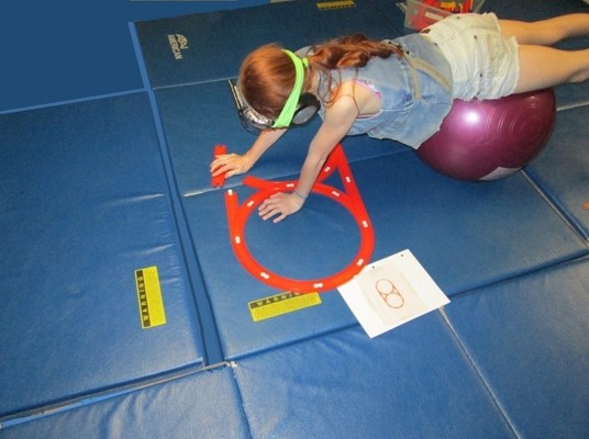 For example,  this older girl is putting  a train track together from a photo of a  layout during her Physioball exercises.  Once again, the resistive exercise stimulates production of brain chemicals that enhance attention.