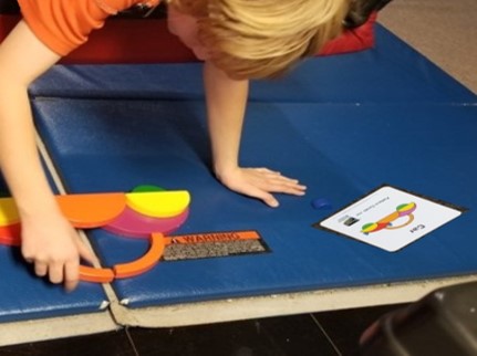 This photo shows a boy walking out on a glider  to arrange parts of a wooden puzzle to match a task card