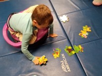 This photo shows a young boy sitting cross legged on a Dizzy Disk, pushing with his arms to reach and assemble a floor puzzle