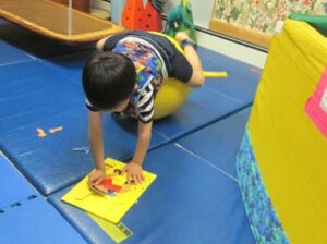 This photo shows a youngster rolling forward onto a Physioball to assemble a puzzle.
