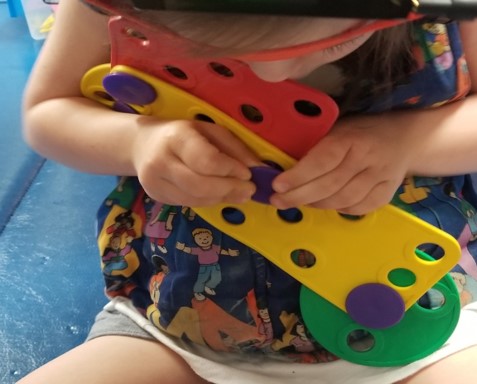 This youngster is also learning to use both hands working together while building a toy with Busy Buttons.  As she holds one part of the toy still with one hand, the other hand is busy pushing and twisting the button into place.