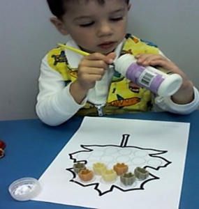 The photo above shows a boy manipulating  his fingertips with a paint brush.  He is twisting the brush to scrape the glue that he needs out of a bottle so he can continue his craft project.