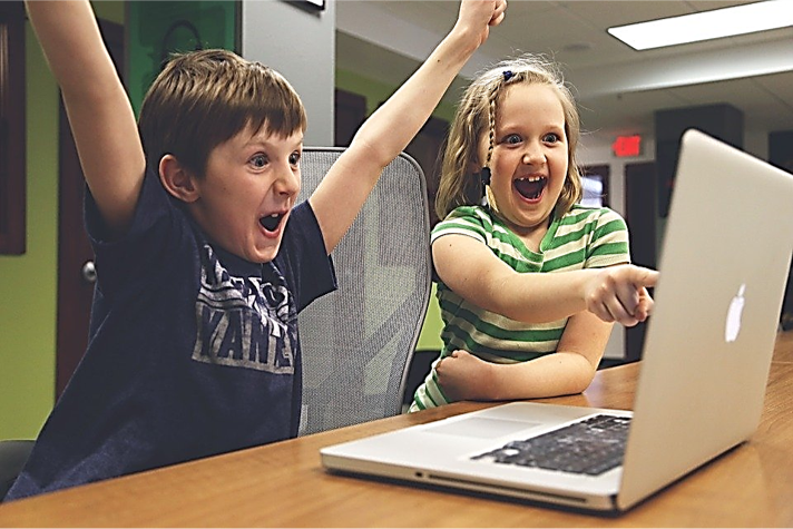 The photo above shows two children looking at a laptop screen.  The boy on the right has his mouth open in a “yes!” posture.  The girl is pointing excitedly at the screen while  laughing joyfully.