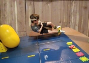 The photo below shows a boy on a tear drop shaped swing turning his body toward a row of foam tiles placed down on a mat.