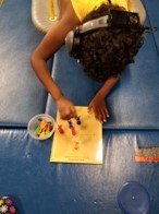 This youngster was able to use ”Sticky Darts” on a glossy dot-to-dot worksheet. He is shown in this photo wearing headphones to heighten his attention and working from a platform swing to arouse his motor sequencing skills. 