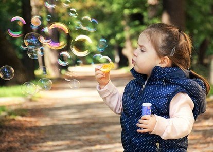 the photo below shows a little girl blowing bubbles She is looking intently on one bubble as she blows it through a bubble wand.