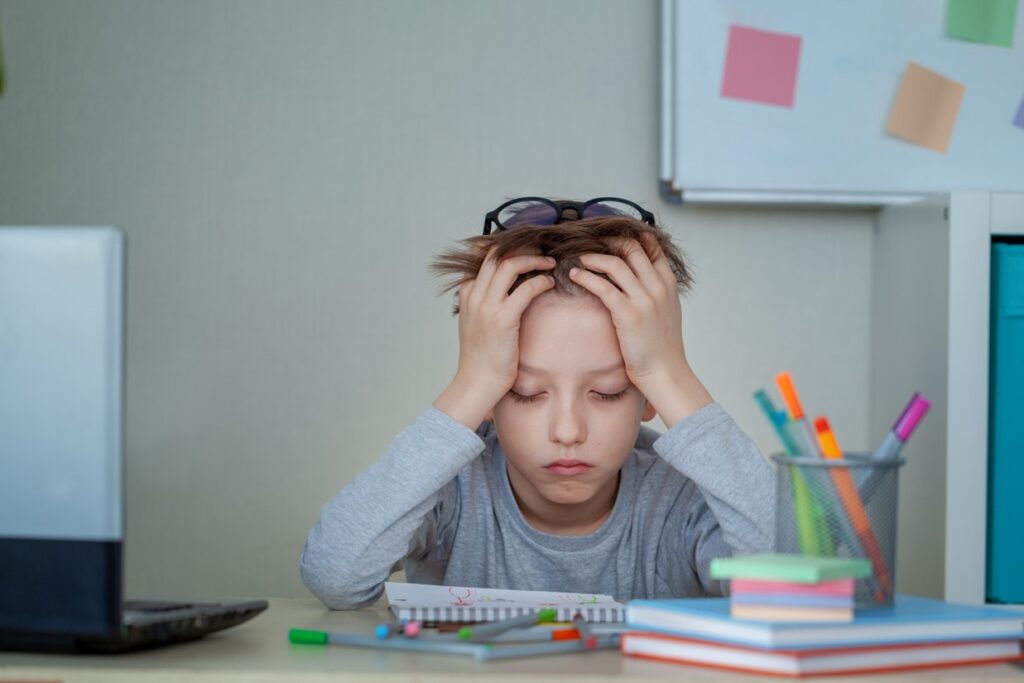 The boy shown in the photo does not have enough energy for the schoolwork shown on his desk.  He is holding his head with both hands and is resting his entire upper body onto his elbows on the desk.